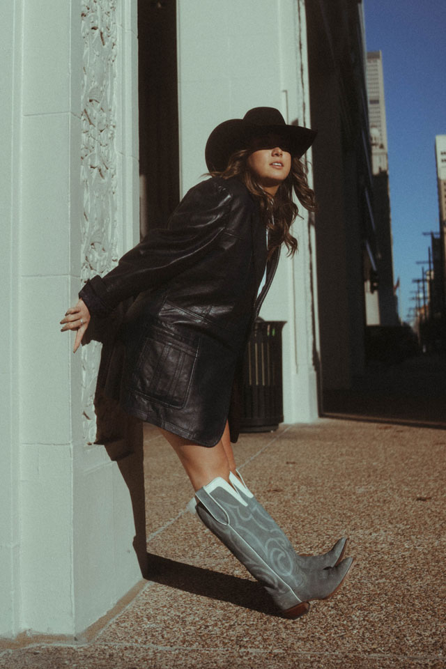 Una mujer con botas Justin Vintage apoyada contra una pared.